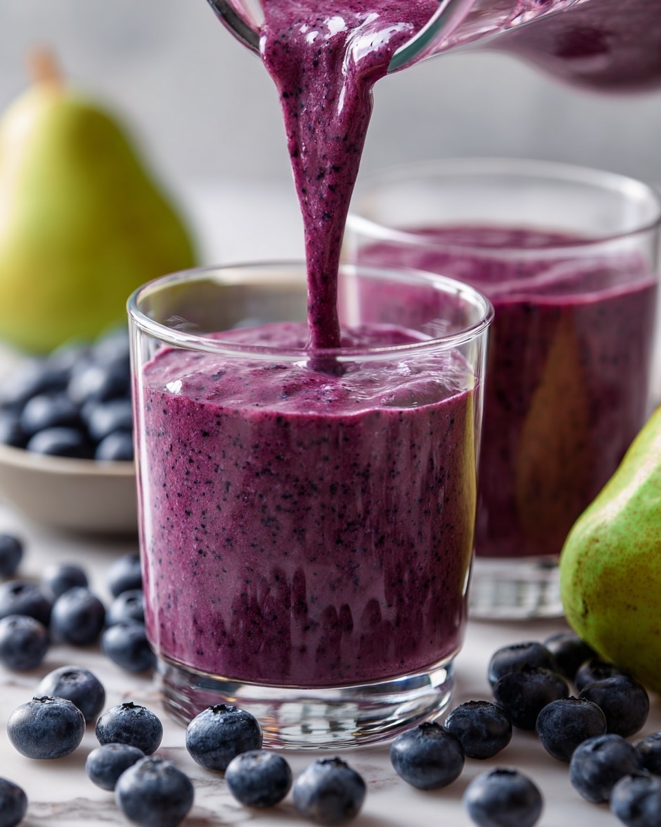 A close-up view of two clear glasses filled with thick, purple blueberry smoothie, one glass being filled with more smoothie from above, showing the smooth flowing texture. The purple smoothie has tiny dark specks in it, hinting at blended blueberries. The glasses sit on a white marbled surface scattered with fresh, round, dark blue blueberries and a green pear on the right side, adding fresh and natural colors to the scene. The background is softly blurred with more blueberries scattered around. Photo taken with an iphone --ar 4:5 --v 7