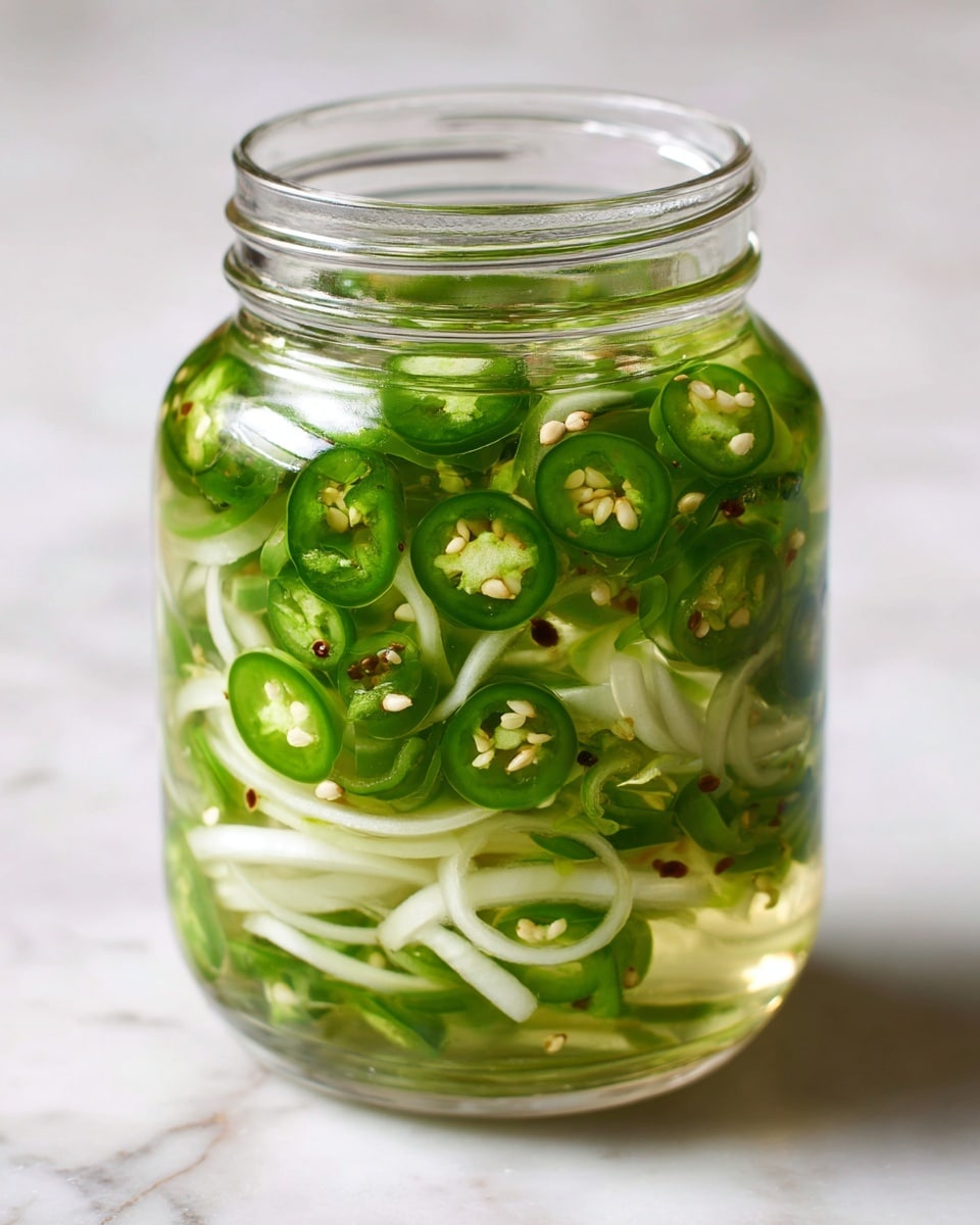 A clear glass jar filled with layers of sliced green jalapeño peppers and thin, white onion strips submerged in clear liquid, with small white seeds from the peppers visible throughout, all placed on a white marbled surface. photo taken with an iphone --ar 4:5 --v 7