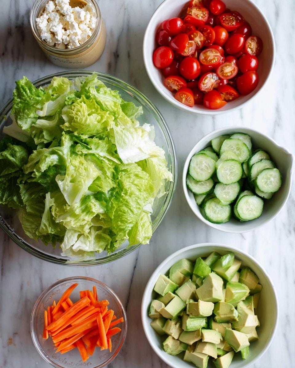 A large clear glass bowl filled with fresh green leafy lettuce sits on a white marbled surface. Above it are two white bowls, one on the left filled with bright red halved cherry tomatoes, and the other on the right filled with light green cucumber slices with dark green edges. To the lower right of the lettuce bowl is a white bowl with chopped light green avocado pieces. Below that is a small clear bowl with thin orange carrot sticks. To the left of the carrots is a small white bowl filled with crumbly white cheese. Above the carrot bowl and to the right is a small clear jar containing light brown salad dressing with visible seeds. All items are arranged neatly on the white marbled texture photo taken with an iphone --ar 4:5 --v 7