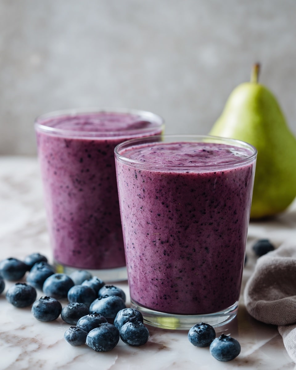 Two clear glasses filled with a thick purple smoothie, rich and creamy in texture, sit on a white marbled surface. The smoothie has tiny dark specks throughout, indicating blended blueberries. Around the glasses, fresh round blueberries are scattered, adding dark blue pops of color. A whole green pear is positioned to the right, contributing a fresh, light green contrast. The scene feels fresh and healthy, with smooth, rounded edges of the glass mixing with the soft fruit shapes. photo taken with an iphone --ar 4:5 --v 7