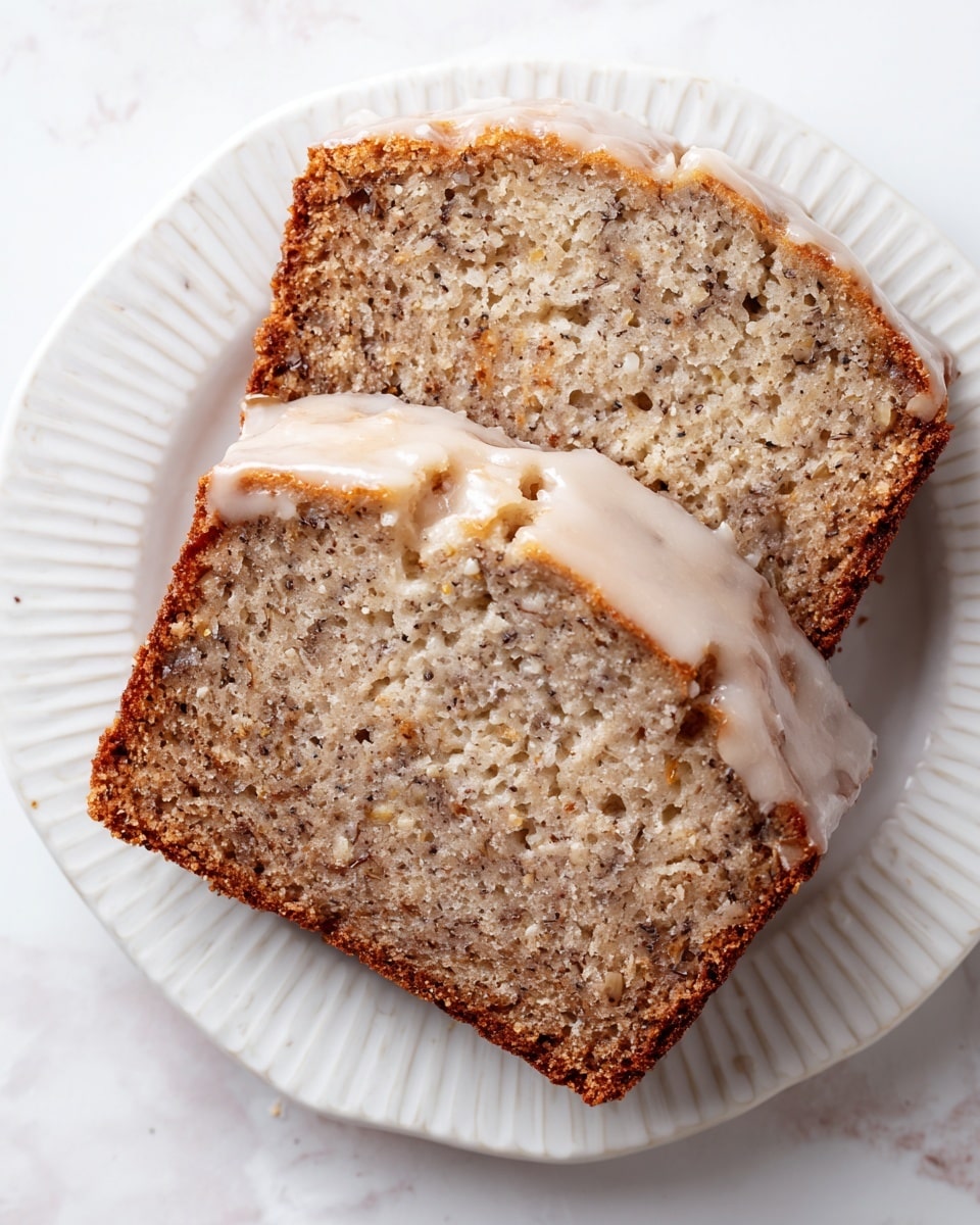 Two slices of banana bread are placed on a white plate with a simple, patterned edge. The banana bread has a moist texture with visible bits of banana and other small specks throughout. The top layer is covered with a smooth, light beige glaze that cracks slightly. The background features a white marbled texture, giving a clean and bright look to the image. photo taken with an iphone --ar 4:5 --v 7