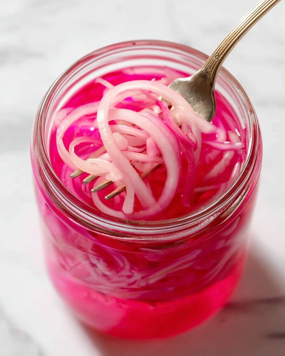 A close-up view inside a clear glass jar filled with thin, pale pink pickled onion slices submerged in bright pink liquid. A metal fork is lifting some of the long, curly onion pieces out of the liquid, showing their smooth, slightly translucent texture. The jar sits on a white marbled surface with soft natural light highlighting the vibrant pink tones of the pickled onions and liquid. photo taken with an iphone --ar 4:5 --v 7