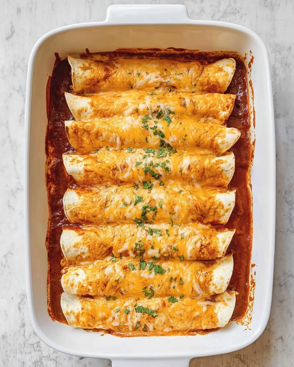 This image shows a white rectangular baking dish filled with ten rolled tortillas arranged in two neat rows of five. Each tortilla is covered with a layer of melted orange cheese that has a smooth and slightly bubbly texture. Beneath the tortillas, there is a visible layer of red sauce that slightly pools around the edges of the dish, adding a glossy contrast. Small green herb pieces are sprinkled unevenly across the top of the cheese. The baking dish is placed on a white marbled surface, enhancing the warm colors of the dish. Photo taken with an iphone --ar 4:5 --v 7