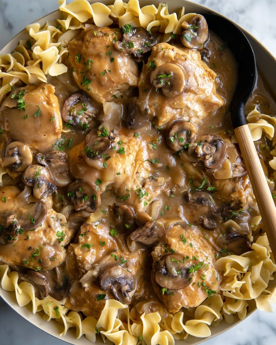 The dish shows several round chicken pieces layered with a thick, light brown sauce that covers them smoothly. Scattered among the chicken are sliced mushrooms with dark brown caps and creamy undersides, adding a soft texture. Mixed in and around are curly, pale yellow egg noodles, some peeking out from under the sauce. Small green parsley flakes are sprinkled over everything, giving a touch of fresh color. The background has a clean white marbled texture, and a black ladle with a light wooden handle rests partially in the dish. Photo taken with an iphone --ar 4:5 --v 7