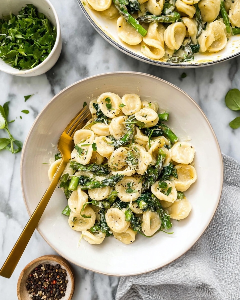 A white bowl holds a creamy pasta dish with orecchiette pasta, bright green asparagus pieces, and dark green spinach leaves mixed throughout. The pasta is coated in a light cream sauce and sprinkled with chopped fresh herbs and black pepper bits. A gold fork rests inside the bowl, and the bowl is placed on a white marbled surface. Above it, a white skillet contains more of the pasta with cream sauce and vegetables, and to the left, a small white bowl holds chopped fresh herbs. There is a light gray cloth near the bowls and some peppercorns in a small dish on the marble. Photo taken with an iphone --ar 4:5 --v 7