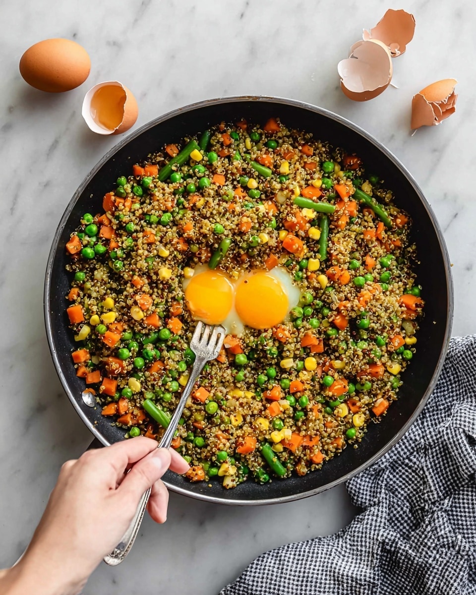 A black pan sits on a white marbled surface with cooked quinoa mixed with green peas, chopped orange carrots, corn kernels, and green beans filling most of the pan on the left side. On the right side inside the pan is a raw egg yolk and a smaller amount of egg white being broken and stirred by a silver fork held by a woman's hand coming in from the bottom right. Three brown broken eggshells rest on the white marbled surface near the top right, and a black-and-white checkered cloth peeks in from the bottom right corner. photo taken with an iphone --ar 4:5 --v 7