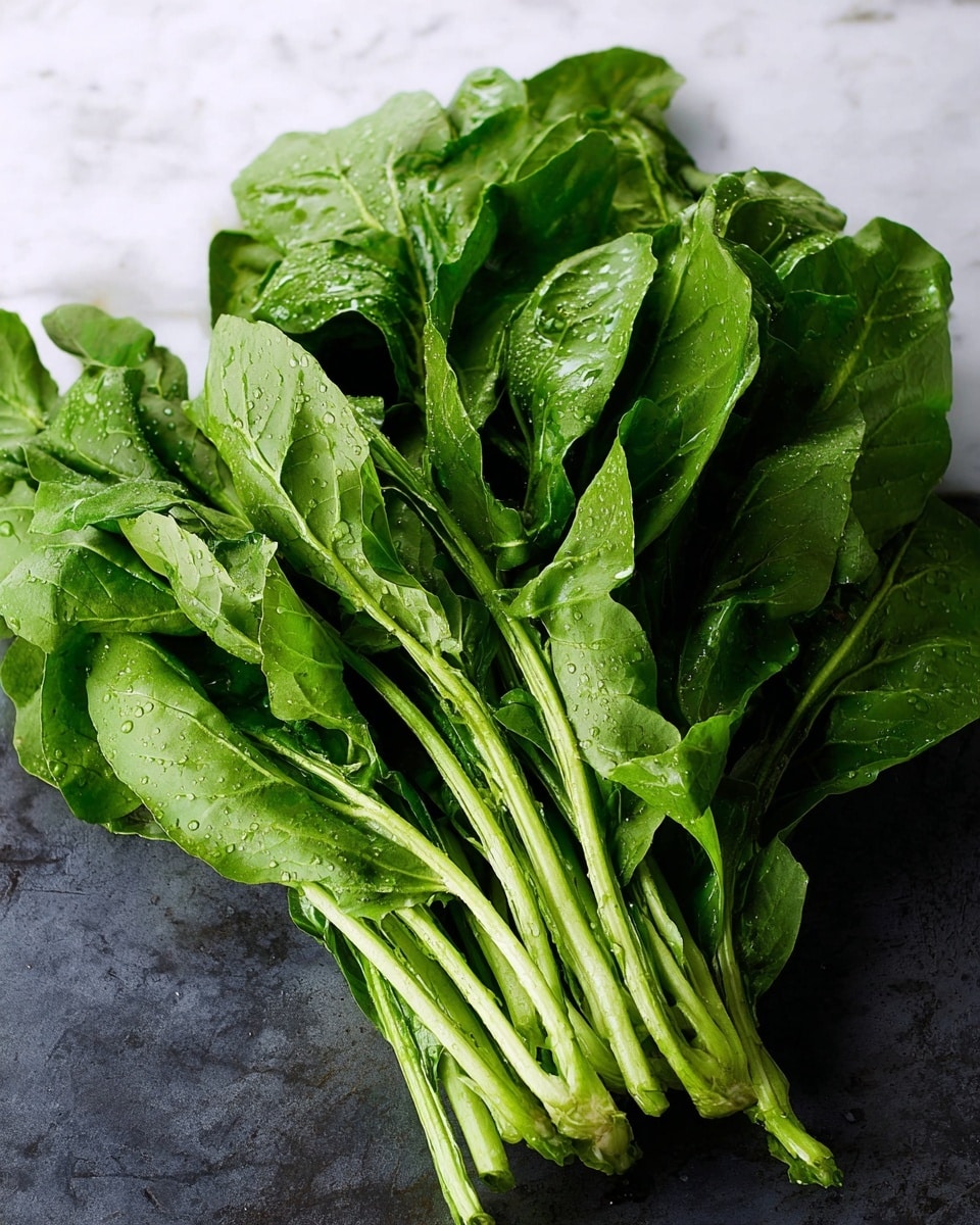A pile of fresh green leafy vegetables with thick pale green stems and broad, slightly wrinkled dark green leaves. The leaves and stems are closely packed together, showing natural texture and water droplets that make them look fresh. The pile is placed on a white marbled surface, providing a clean and bright background, highlighting the vibrant green color of the vegetables. photo taken with an iphone --ar 4:5 --v 7