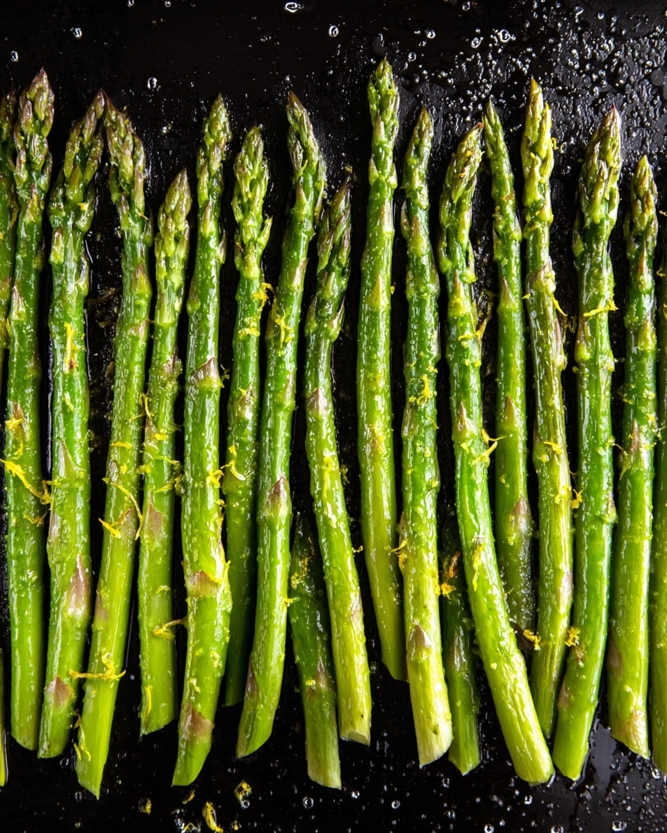 A single layer of bright green asparagus spears is lined up closely side by side on a dark baking tray. Each spear has a slightly shiny texture showing they are coated with oil. The tips are a bit darker green and some show tender purple hints, while the stalks have a few light brown spots indicating roasting. Small bits of grated yellow zest and sprinkled seasoning are scattered lightly over the spears, adding texture contrast. The tray surface has small droplets of oil and slight reflections, emphasizing the cooked look, and the background is a white marbled texture. photo taken with an iphone --ar 4:5 --v 7