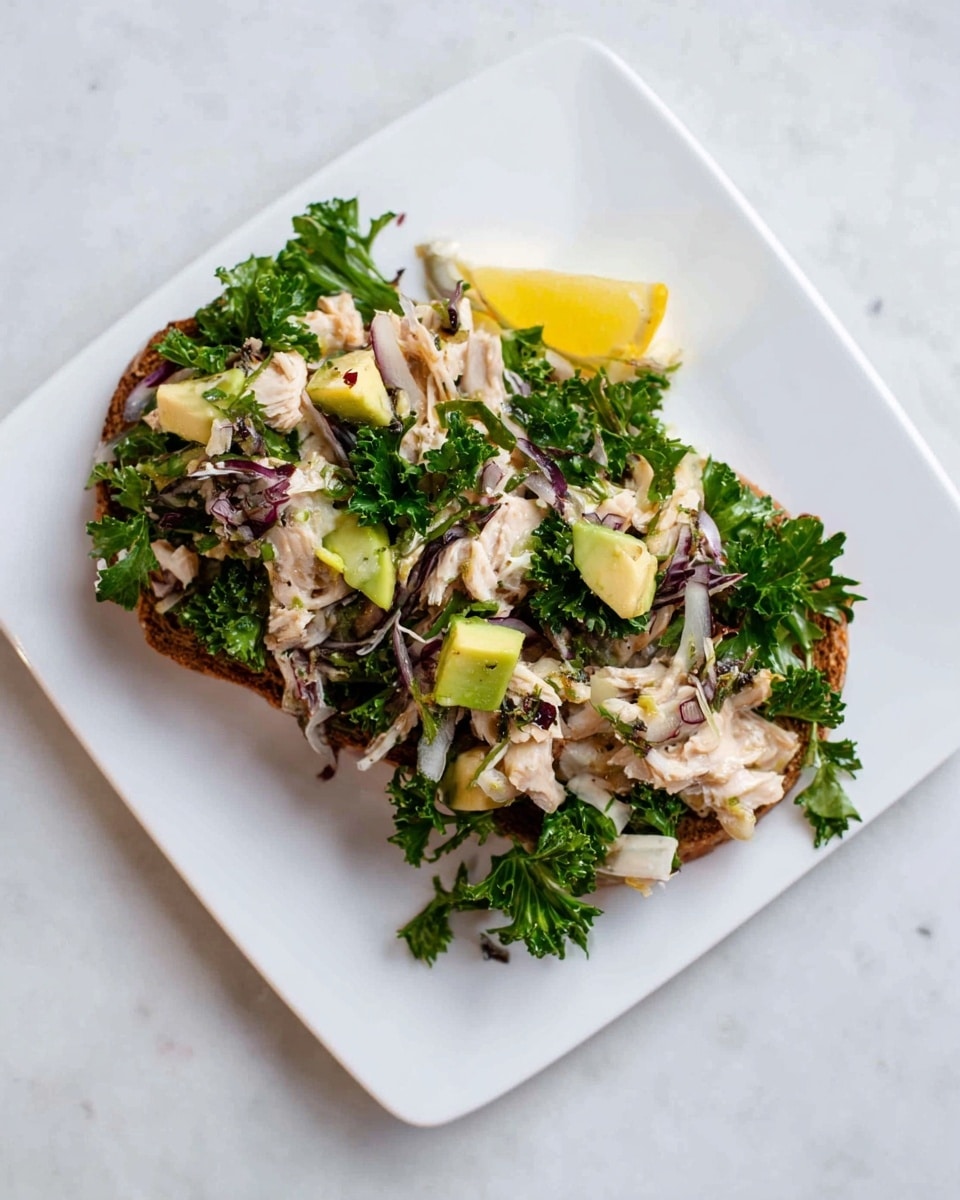 A white square plate holds a dish with two layers: the base is a dark brown toasted bread slice, topped with a mix of shredded light beige meat, leafy green parsley, light purple thin onion slices, and small yellow-green avocado chunks. The ingredients are spread unevenly, showing a fresh and natural texture. The plate sits on a white marbled surface. photo taken with an iphone --ar 4:5 --v 7