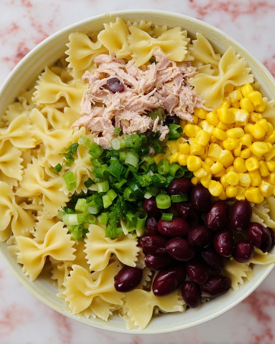 This image shows a bowl of farfalle pasta as the base layer, light yellow in color with a smooth texture. On top of the pasta, there is a layer of bright yellow corn at the bottom right, a small pile of shredded light pink tuna on the left, and dark purple olives scattered mostly on the top right. In the middle, chopped green onions add a pop of green color. All ingredients are placed in a white bowl sitting on a white marbled surface. photo taken with an iphone --ar 4:5 --v 7