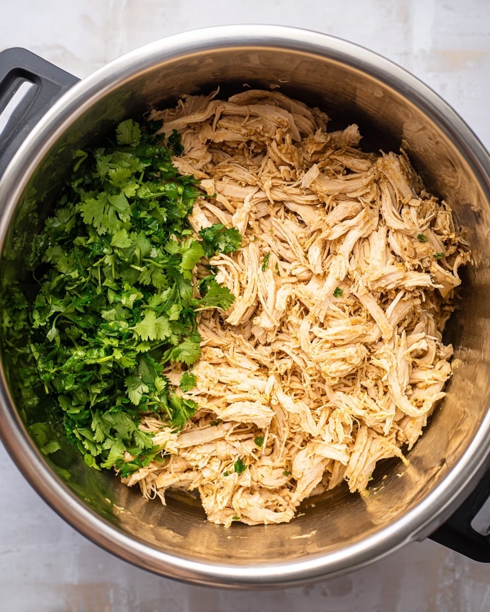 The image shows a close-up of a stainless steel pot filled with shredded light golden cooked chicken. The chicken forms most of the dish with a soft, fibrous texture. On one side of the pot, there is a fresh bunch of bright green chopped cilantro, providing a contrasting color and fresh look. The pot has dark handles, and the background is a white marbled texture. photo taken with an iphone --ar 4:5 --v 7