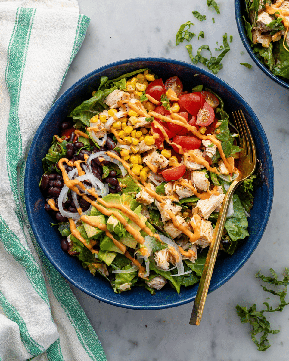 A blue bowl holds a fresh salad with several layers: the first layer is mixed dark green leafy vegetables, the second layer has diced white chicken pieces, bright yellow corn kernels, and sliced red cherry tomatoes, and the third layer shows thin white onion strips and black beans scattered throughout. A light orange dressing is drizzled on top, adding a creamy texture. A gold fork rests inside the bowl. The bowl is placed on a white marbled surface next to a white and green striped cloth napkin. Small green herb leaves are scattered around the bowl. Photo taken with an iphone --ar 4:5 --v 7
