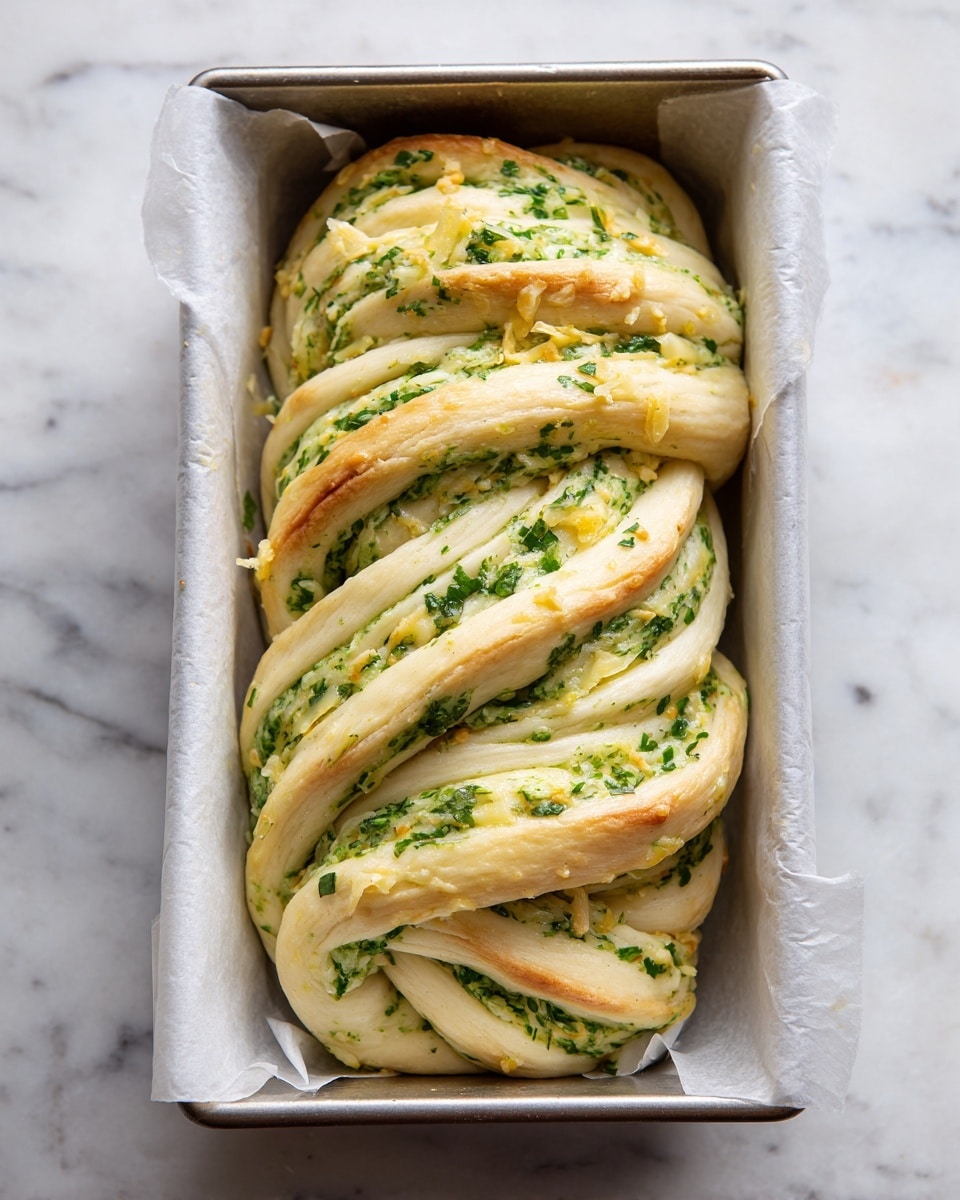 The image shows an unbaked braided loaf twisted inside a silver rectangular baking pan lined with white parchment paper. The braided dough has several thick layers, each filled with a green herb mixture and sprinkled with light yellow shredded cheese. The layers show a mix of creamy dough color and bright green, giving the loaf a textured and swirled look. The pan sits on a white marbled surface. photo taken with an iphone --ar 4:5 --v 7
