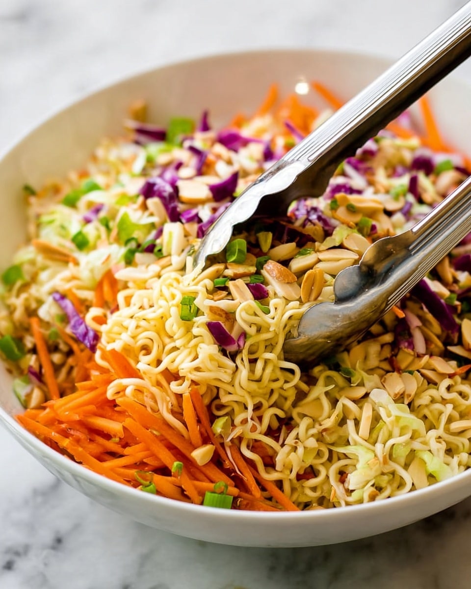 A white bowl filled with a colorful salad shows three main layers: the base layer has light yellow dry ramen noodles with a wavy texture, on top there is a mix of thin, long orange carrot sticks and crunchy light brown slivered almonds scattered around, and the top layer features small pieces of green onion and some shredded cabbage, both purple and white, giving a fresh look. Silver metal tongs are holding some of the salad from the side of the bowl. The bowl sits on a white marbled surface. photo taken with an iphone --ar 4:5 --v 7