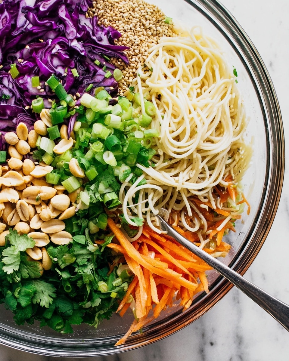 This image shows a clear round bowl filled with layers of colorful food on a white marbled surface. The bottom layer has finely sliced purple cabbage with light veins, topped on the left with chopped green spring onions that are bright and fresh. Above this layer, there are thick white spaghetti noodles curled on the right middle side, with fresh green chopped cilantro above them. Near the top left corner are whole peanuts and a large pile of light brown sesame seeds. On the far right edge of the bowl, there is a pile of shredded orange carrots mixed with thinly sliced lighter brown vegetables. A silver fork rests on the left inside the bowl, partly in the green onions. photo taken with an iphone --ar 4:5 --v 7