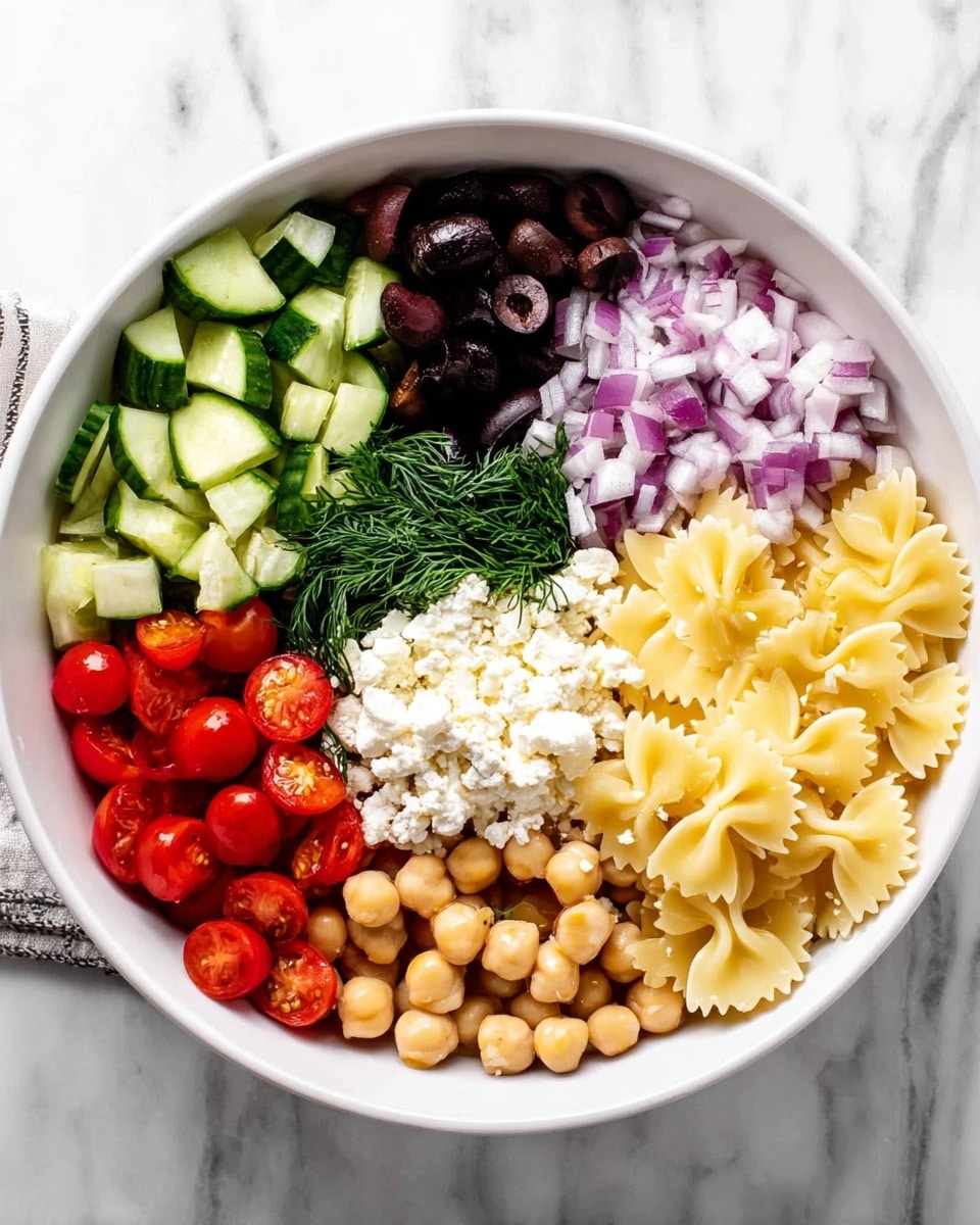 A white bowl sits on a white marbled surface and inside it are seven layers of food arranged side by side. At the top left, there are small green cucumber slices with a smooth, shiny texture. Next to them on the right, finely chopped purple onions show a slightly translucent texture. Next, whole black olives add a deep dark color and smooth look. Below the olives, there is a small bunch of fresh green dill. To the right of the dill, bow-tie shaped cooked pasta is pale yellow with a soft texture. Below the pasta, round light beige chickpeas fill the section with a firm smooth surface. To the left of the chickpeas, bright red cherry tomato halves with a glossy wet look sit next to a pile of crumbly white cheese in the center. The cheese forms a small mound, standing out against the other ingredients. Photo taken with an iphone --ar 4:5 --v 7