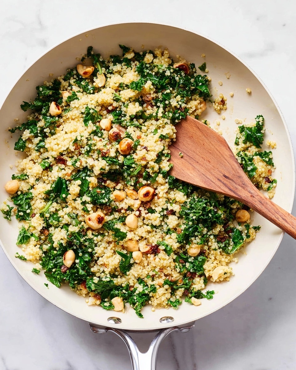 A white pan filled with a mix of fluffy, light yellow quinoa grains, chopped dark green kale leaves, and small, round, light golden brown toasted hazelnuts scattered evenly throughout. A wooden spoon with a light natural wood texture rests partially inside the pan on the right side, with some quinoa grains sticking to it. The pan sits on a white marbled surface. photo taken with an iphone --ar 4:5 --v 7