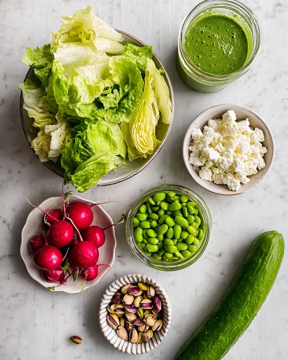 Several small white bowls and a clear bowl are arranged on a white marbled surface. The clear bowl contains layered fresh green and pale yellow lettuce leaves with a crisp texture. One white bowl holds bright green edamame beans, another has red radishes with some dirt still on them, and a third is filled with crumbly white cheese. There is a small bowl with green microgreens, and a white ridged dish contains a handful of pistachio nuts with a mix of green and brown shells. Next to the bowls lies a whole long green cucumber with a shiny, smooth skin. A small glass jar filled with vibrant green sauce is also placed on the surface. Photo taken with an iphone --ar 4:5 --v 7