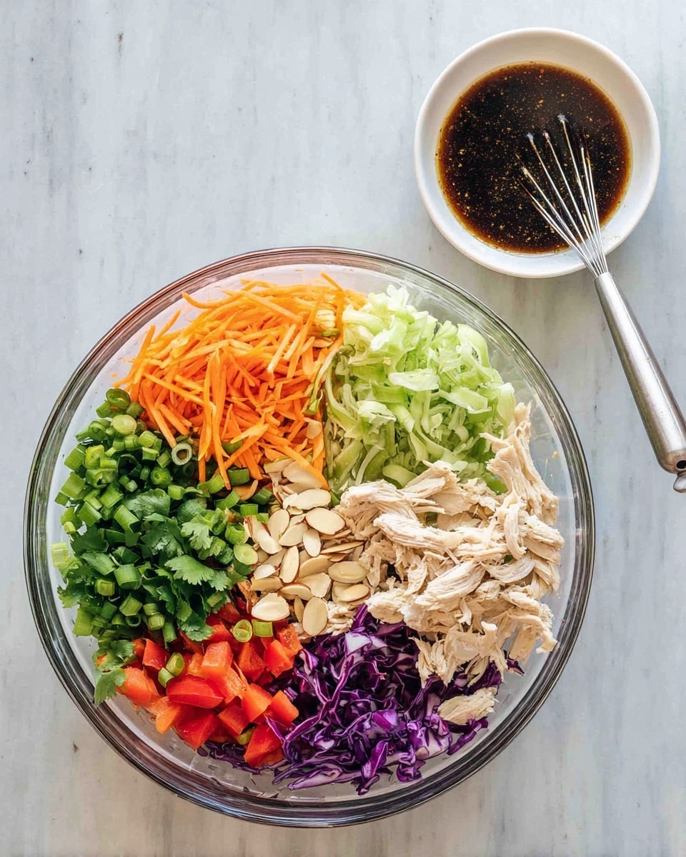 A clear glass bowl is filled with a colorful layered salad on a white marbled surface. Starting at the top left, there are chopped green onions in bright green, next to them are shredded orange carrots, and beside the carrots is fresh green cilantro. Below the cilantro, there are light beige shredded chicken pieces. To the right of the chicken, thin light green slices of vegetable are visible. The bottom layer includes bright red bell pepper strips and sliced almonds in off-white with specks of brown, along with shredded purple cabbage on the bottom left. Above the bowl, a small white bowl holds dark brown dressing with a small whisk resting inside. Photo taken with an iphone --ar 4:5 --v 7