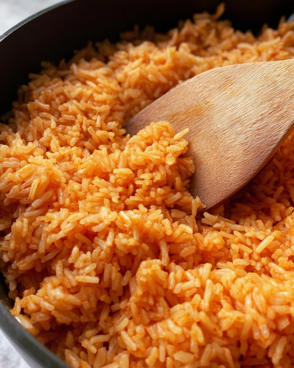 The image shows a close-up of orange-colored cooked rice in a black pot. The rice grains look soft and fluffy, with a slightly oily texture. A wooden spoon with a smooth surface is partly buried in the rice on the right side, gently pushing the rice. The background is a white marbled texture. photo taken with an iphone --ar 4:5 --v 7