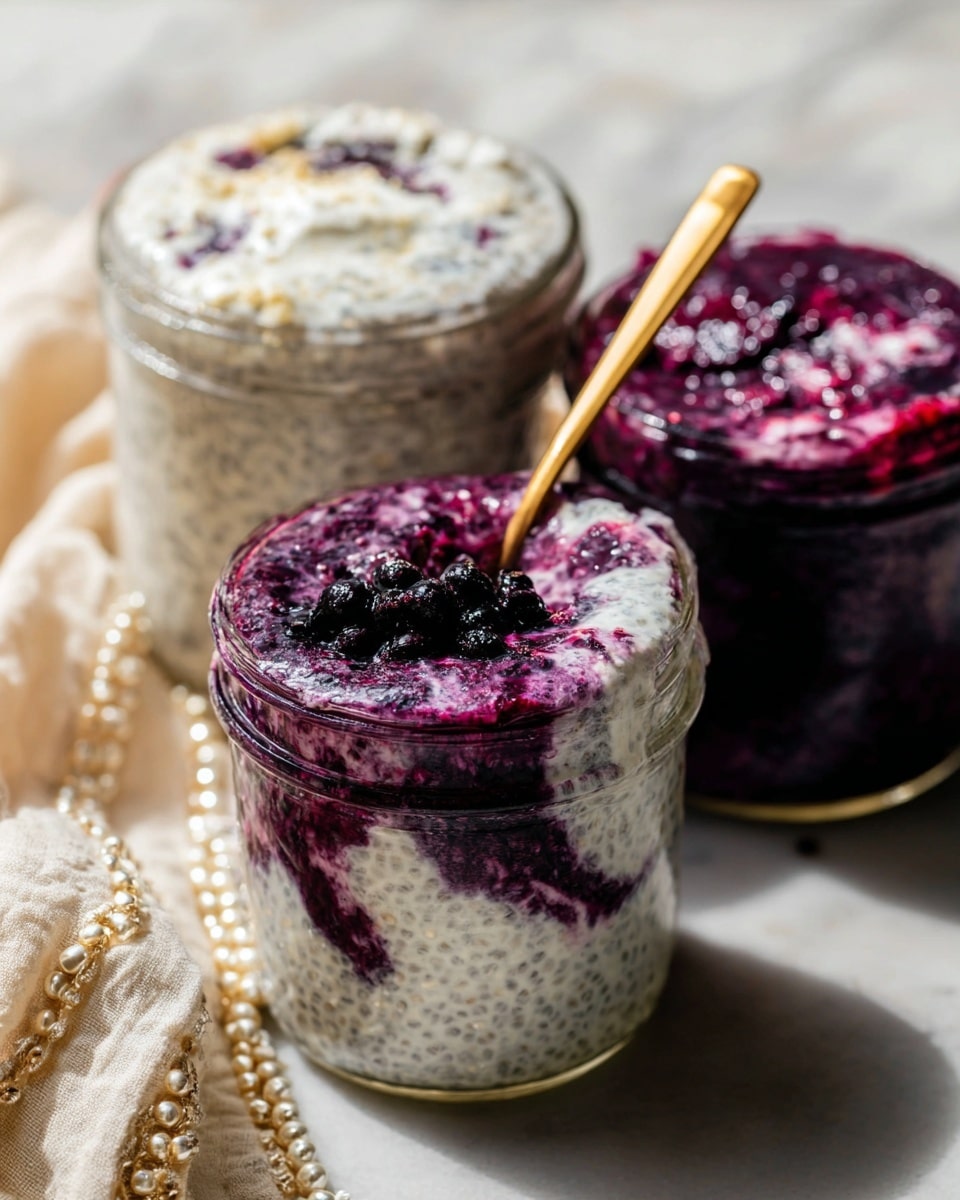 A clear glass bowl sits on a wooden board with a blue and white cloth to the side and a white marbled surface in the background. Inside the bowl, there are three visible layers: the bottom layer is deep purple from blueberry sauce, the middle layer is creamy white textured chia pudding, and the top layer is a mix of whole dark blueberries and purple blueberry sauce that partly covers the pudding. A gold spoon is partially dipped in the bowl, lifting some pudding with blueberry sauce and berries. Some loose blueberries are scattered on the white marbled surface near the bowl. Photo taken with an iphone --ar 4:5 --v 7