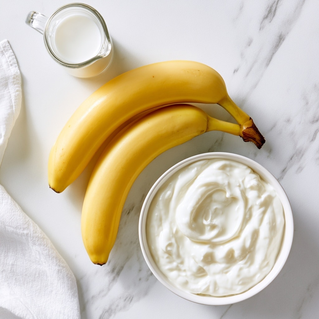 Two whole yellow bananas lie parallel on a white marbled surface, with the larger one at the top and the smaller one below it. Above the bananas is a small clear glass pitcher filled with white milk. Below the bananas is a round white bowl filled with thick, smooth white Greek yogurt. A white cloth is partly visible on the left side of the image. photo taken with an iphone --ar 4:5 --v 7