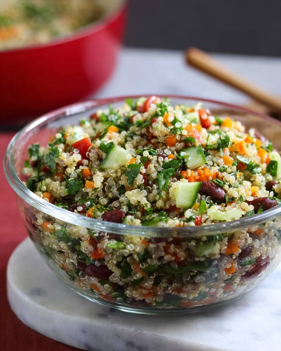 A clear glass bowl is filled with a colorful quinoa salad that shows many small layers mixed together. The bottom layers have tiny pale quinoa grains combined with dark brown beans, green parsley, and small pieces of red tomato. Above this, more quinoa grains are mixed with bright green cucumber slices, orange carrot bits, and more chopped herbs. The salad is piled high with pieces of green herbs and bits of red and orange vegetables on top. The bowl sits on a white marbled surface, with a blurred red pan in the background. photo taken with an iphone --ar 4:5 --v 7