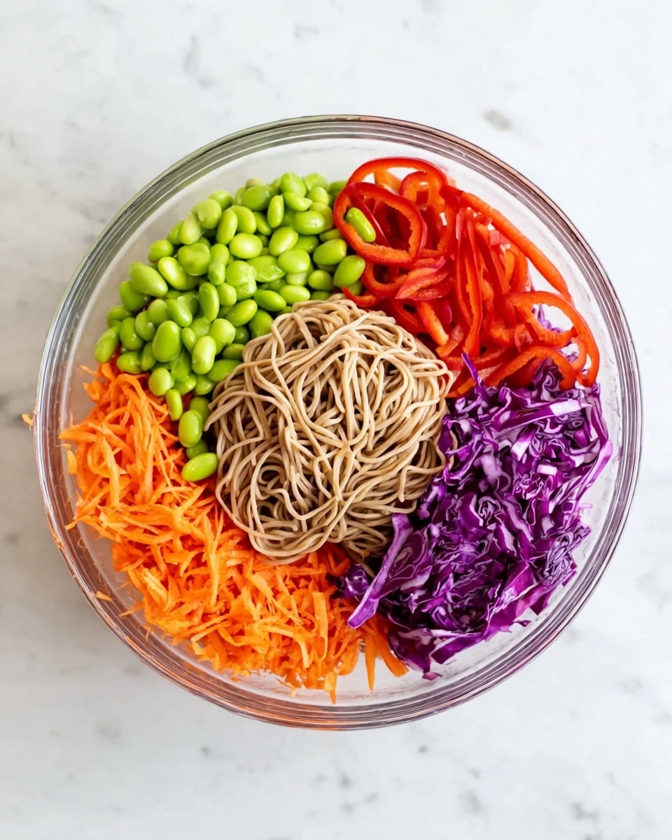 In a clear round glass bowl placed on a white marbled surface, there are five distinct sections of ingredients arranged separately. Starting from the bottom middle, there is a layer of light brown noodle strands forming a loose mound. Moving clockwise, bright red thin strips of bell pepper are neatly piled on the right side of the bowl. Next, at the top right, there is a layer of shredded purple cabbage with a crisp texture. At the top left of the bowl, a cluster of green edamame beans adds a fresh look. Finally, the bottom left is filled with finely shredded orange carrots, creating a colorful and healthy mix. The layers are all fresh and vibrant, cleanly separated in the bowl. Photo taken with an iphone --ar 4:5 --v 7