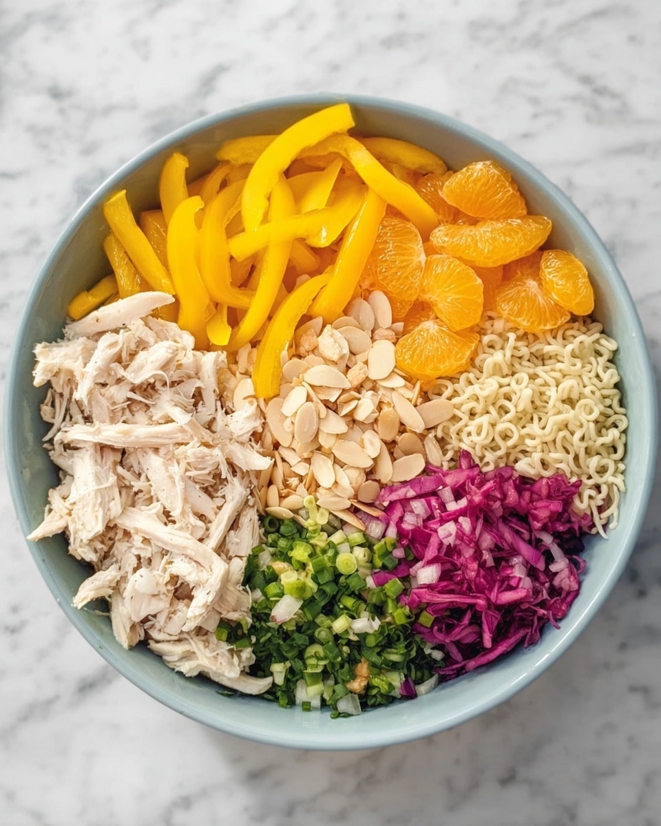 A large white bowl holds a colorful, organized salad with eight visible sections. Starting from the top left and moving clockwise, there are bright yellow sliced bell peppers, shredded white chicken, shiny mandarin orange slices, thinly sliced almond pieces, finely chopped green herbs, pickled purple onion rings, chopped green onions, and a cluster of dry pale ramen noodles. In the center, there is a small pile of mixed shredded cabbage showing white and purple colors. The bowl sits on a white marbled surface. Photo taken with an iphone --ar 4:5 --v 7