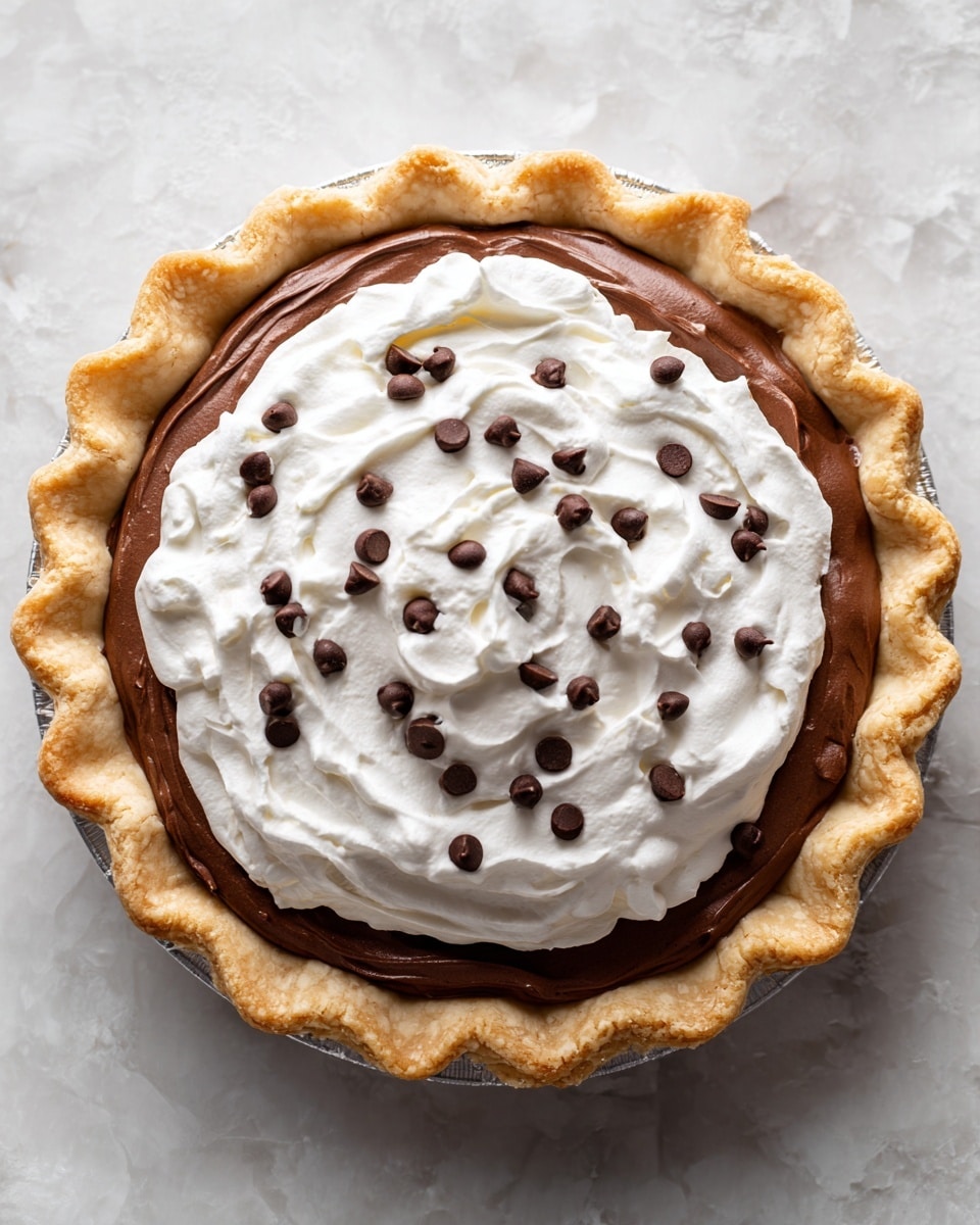 A round pie with a golden brown crust forms the base layer, filled with a smooth, rich dark brown layer of chocolate pudding. On top, there is a thick layer of fluffy white whipped cream spread evenly in a circular shape. Scattered across the whipped cream are small, dark brown chocolate chips, adding texture and contrast. The pie sits on a white marbled surface. photo taken with an iphone --ar 4:5 --v 7