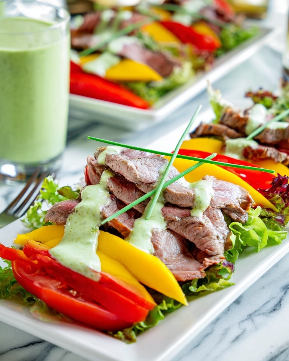 The dish shows a white rectangular plate with a base layer of mixed green leafy lettuce. On top of the lettuce, there are thick slices of yellow mango arranged in a row. Over the mango slices, there are several layers of thinly sliced cooked beef, showcasing a light brown to pinkish color with a tender texture. On the sides of the beef, there are bright red tomato slices. The dish is topped with a light green creamy sauce drizzled unevenly across the beef. A single green chive stem crosses the top as garnish. In the background, there is another plate with the same dish and a glass with a green creamy drink on a white marbled surface. Photo taken with an iphone --ar 4:5 --v 7