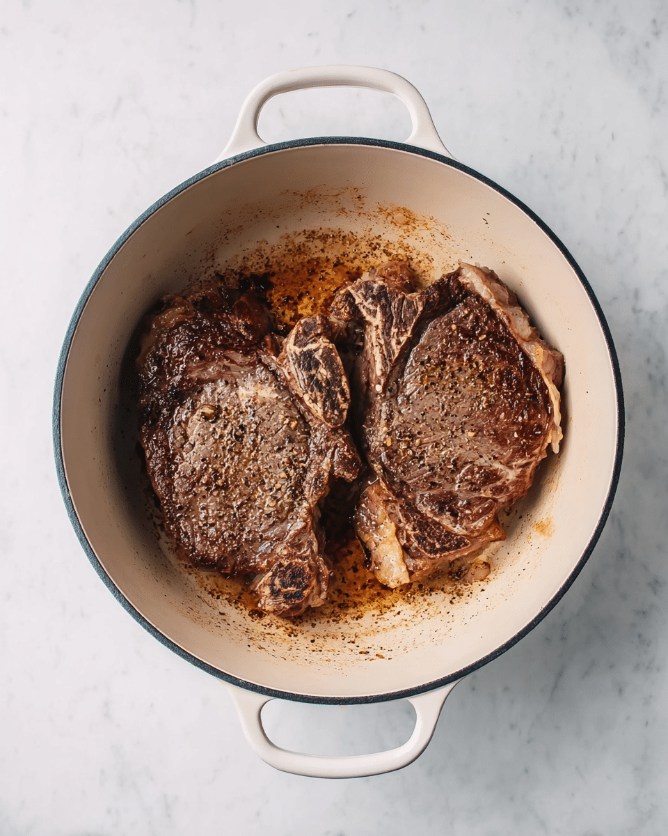 Two cooked steaks with a brown and slightly pink color, showing a textured surface with seasoning visible on top, lying flat inside a white pot with handles on each side. The steaks have some fat edges, and there is a small amount of juice and browned bits around them inside the pot. The pot is placed on a white marbled surface. photo taken with an iphone --ar 4:5 --v 7
