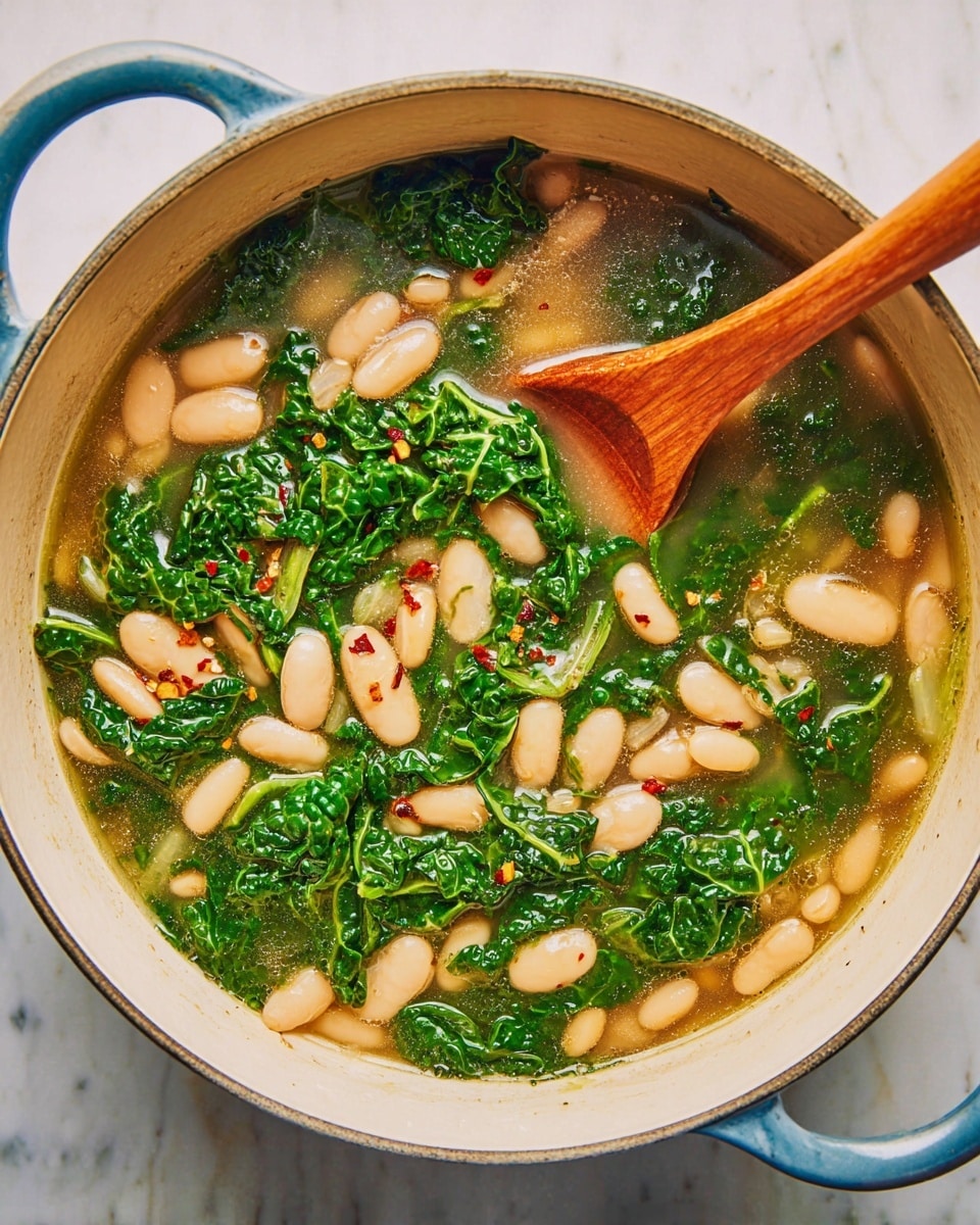 A large white pot filled with a light broth soup that has three main layers: at the bottom, pale beige white beans; in the middle, bright green leafy kale pieces scattered evenly; and on top, clear broth with small bits of onion and red chili flakes. A wooden spoon rests diagonally inside the pot, the spoon part sitting on top of the soup near the center. The pot handle is visible on the right side, and the pot sits on a white marbled surface with soft natural lighting. photo taken with an iphone --ar 4:5 --v 7