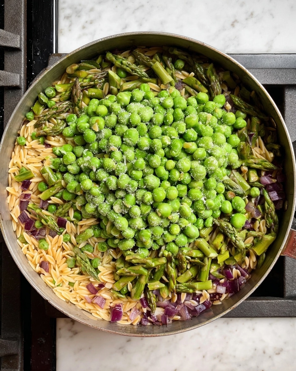 In a round metal pan, there is a colorful mix of food layered in parts: the bottom layer is a light brown orzo pasta mixed with small pieces of purple onion scattered evenly around the edge, the middle layer consists of bright green asparagus pieces cut into short segments spread throughout the pasta, and on top, there is a thick pile of frozen green peas at the center, some of which have a light frost covering. The pan sits on a black stove, and the scene is set on a white marbled surface. photo taken with an iphone --ar 4:5 --v 7