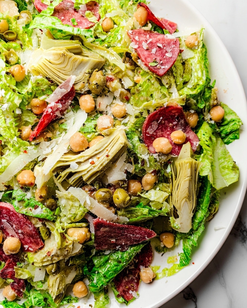 A close-up of a salad on a white plate with a white marbled background, showing a mix of green shredded lettuce as the base layer, topped with sliced artichoke hearts that are light green and textured, round chickpeas scattered throughout, thin slices of red salami spread unevenly across, small bits of white shredded cheese sprinkled on top, and a light dressing coating some leaves adding a shiny texture. photo taken with an iphone --ar 4:5 --v 7