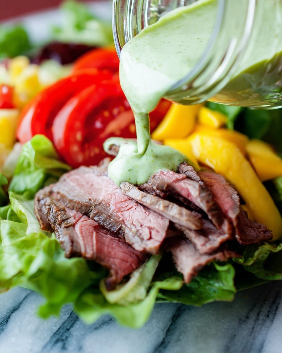 The image shows a close-up of a fresh salad with four layers. The bottom layer is green leafy lettuce with a crisp texture. On top of this is a layer of thick red tomato slices. Above the tomatoes are slices of yellow mango, and then on top are several thin pieces of sliced roast beef colored brown with some pink in the middle. A green creamy sauce with a smooth texture is being poured over the roast beef from a small clear glass jar with a woman's hand holding it. The dish is placed on a surface with a white marbled texture. photo taken with an iphone --ar 4:5 --v 7