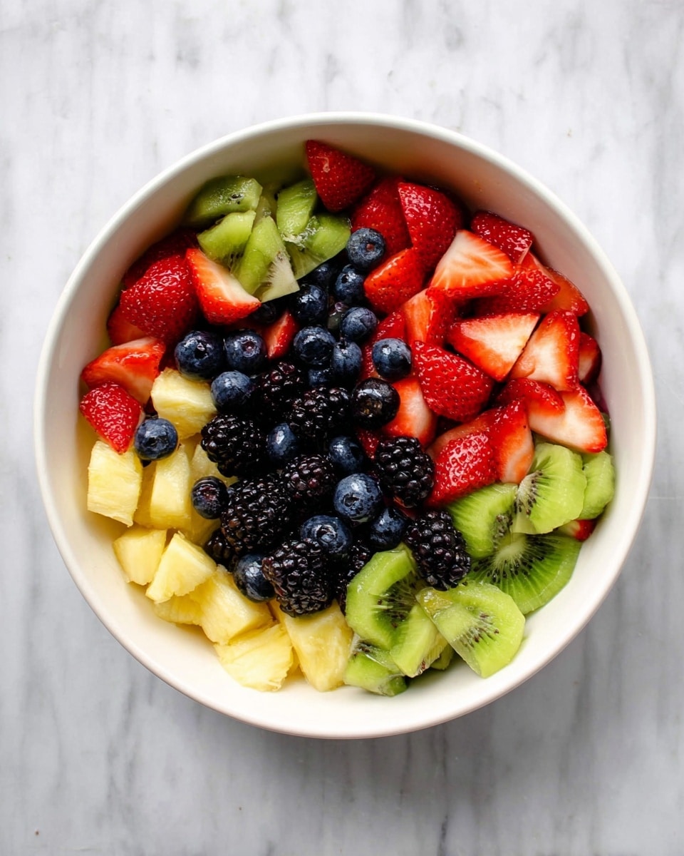 A white bowl filled with a colorful mix of fruit pieces is shown on a white marbled surface. The fruit mix has five visible layers: the bottom layer has light yellow chunks of pineapple, the middle layer holds many dark blackberries, the next layer includes some bright green kiwi slices, the fourth layer has fresh whole blueberries scattered on top, and the top layer shows red strawberry halves dispersed evenly around the bowl. The fruits have different textures, with the soft strawberries and blueberries contrasting with the firmer pineapple and kiwi slices. photo taken with an iphone --ar 4:5 --v 7