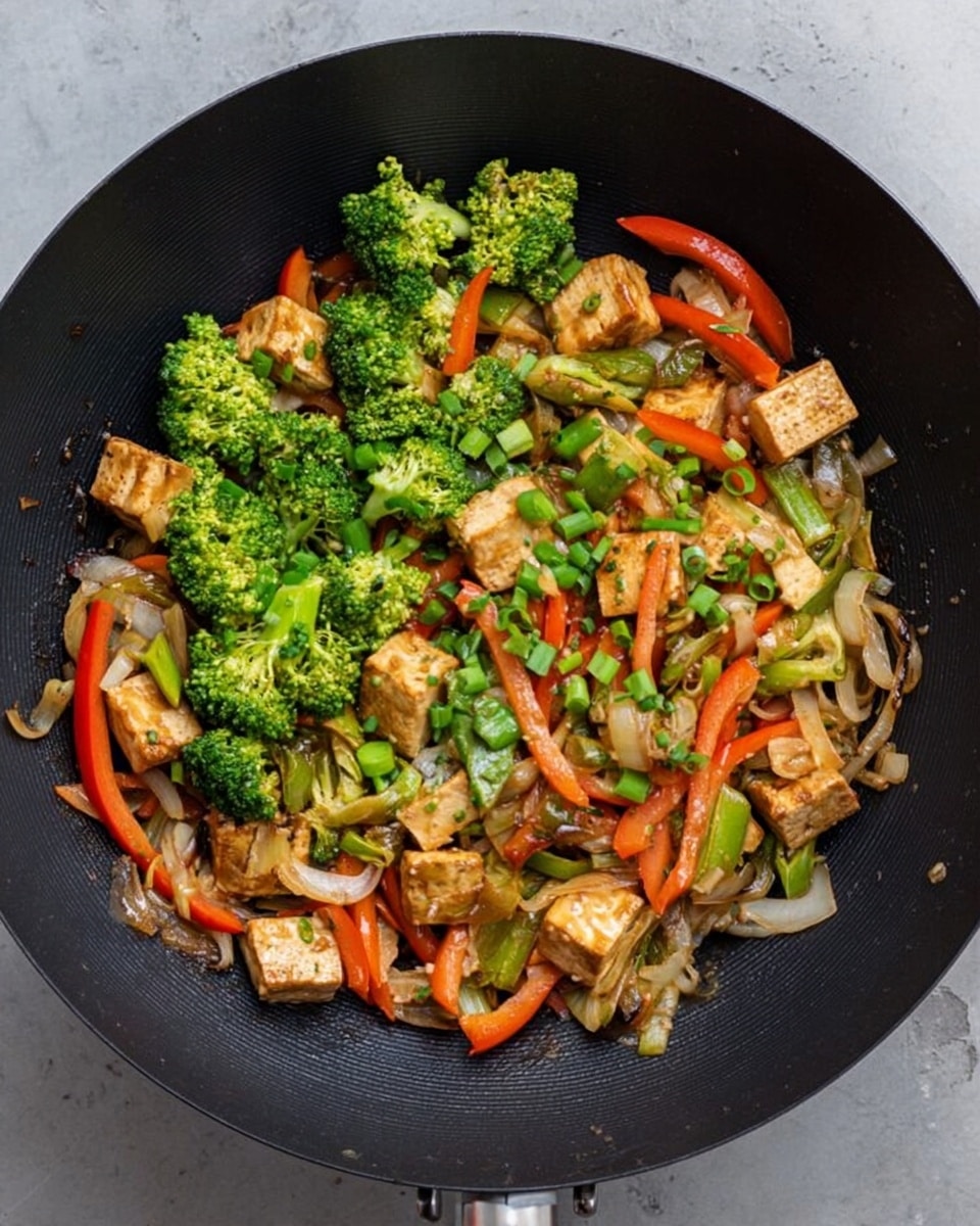 The image shows a black wok filled with stir-fried vegetables and tofu. The dish has several layers: bright green broccoli florets scattered on top and through the mix, light brown tofu pieces with a slight shine spread evenly, thin translucent onion slices, and long, thin red bell pepper strips. There are also finely chopped green onions sprinkled on top, adding a fresh green contrast. The wok is placed on a white marbled surface that brightens the scene. The overall look is colorful, fresh, and inviting, with the mix of textures visible in the vegetables and tofu. photo taken with an iphone --ar 4:5 --v 7