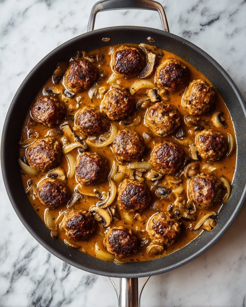 A large black pan on a white marbled surface holds about twenty browned meatballs evenly spread throughout a thick brown sauce with visible slices of mushrooms and onions, the sauce coating the meatballs and filling the spaces in between, and the pan's silver handle extending downward in the image; photo taken with an iphone --ar 4:5 --v 7
