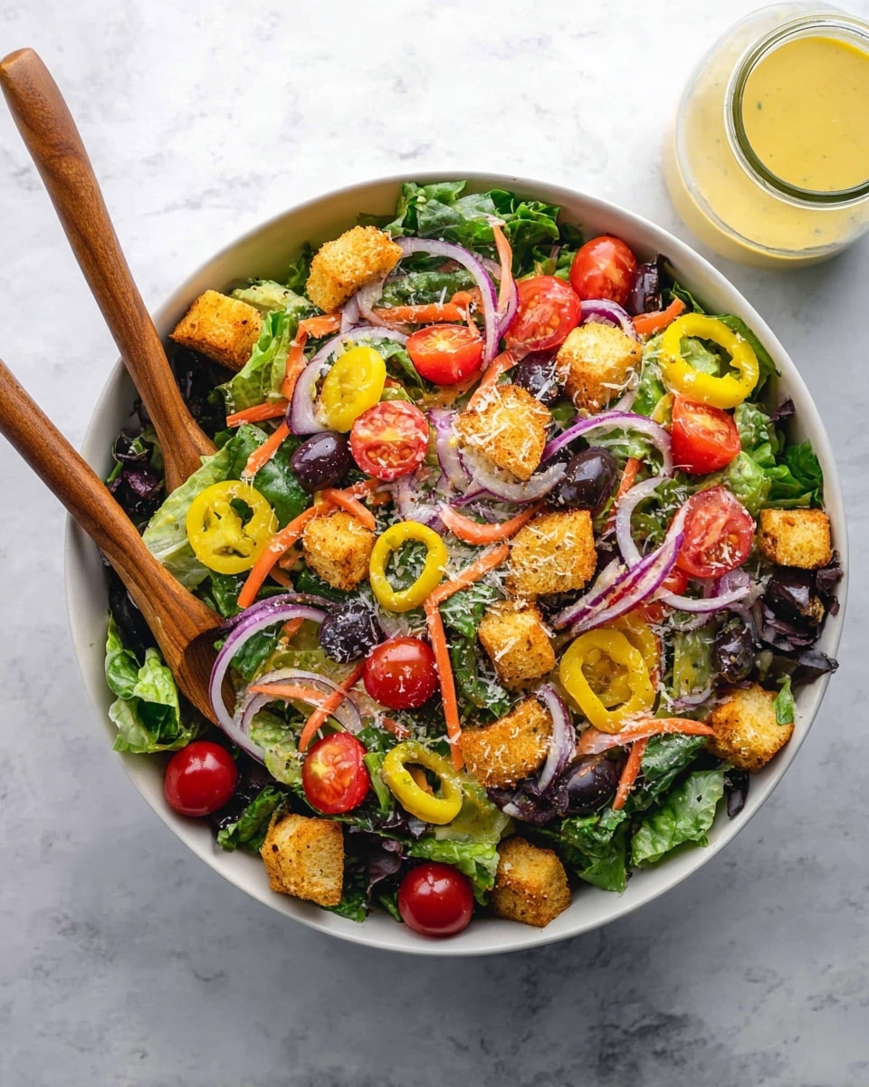 A white bowl filled with a fresh salad featuring a base layer of mixed green lettuce leaves, topped with bright red halved cherry tomatoes and scattered dark black olives. Thin purple rings of onion are layered throughout, along with small, crunchy golden-brown croutons resting on top. Yellow pepperoncini peppers sit on the side, adding a bright pop of color. There is a light drizzle of creamy dressing over the salad, with a hint of grated cheese sprinkled on top. Two wooden salad spoons rest gently on the side of the bowl, all set on a white marbled surface. A glass jar with yellow dressing is blurred in the background. Photo taken with an iphone --ar 4:5 --v 7