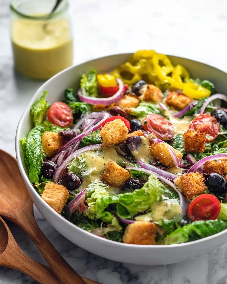 A large white bowl filled with a fresh salad sits on a white marbled surface. The salad has a base layer of green lettuce leaves with strips of carrot mixed in. On top, there are sliced red cherry tomatoes, rings of purple onion, black olives, and bright yellow pepperoncini peppers arranged evenly. Golden brown croutons are scattered across the surface, along with a light sprinkling of grated cheese. Two wooden salad spoons rest in the bowl, one extending out of the bowl to the upper left. To the right of the bowl, a small glass jar with light yellow dressing is placed. Photo taken with an iphone --ar 4:5 --v 7