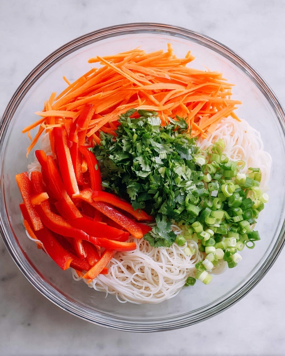A clear glass bowl is filled with four main layers of fresh ingredients arranged separately. The bottom layer shows thin white rice noodles sitting at the base. On top of that, there are bright orange thin carrot sticks placed on one side, with vibrant red bell pepper sticks positioned next to them. A small mound of chopped green onions is on the right side, and in the center lies a pile of chopped green cilantro leaves. The bowl sits on a white marbled surface. photo taken with an iphone --ar 4:5 --v 7