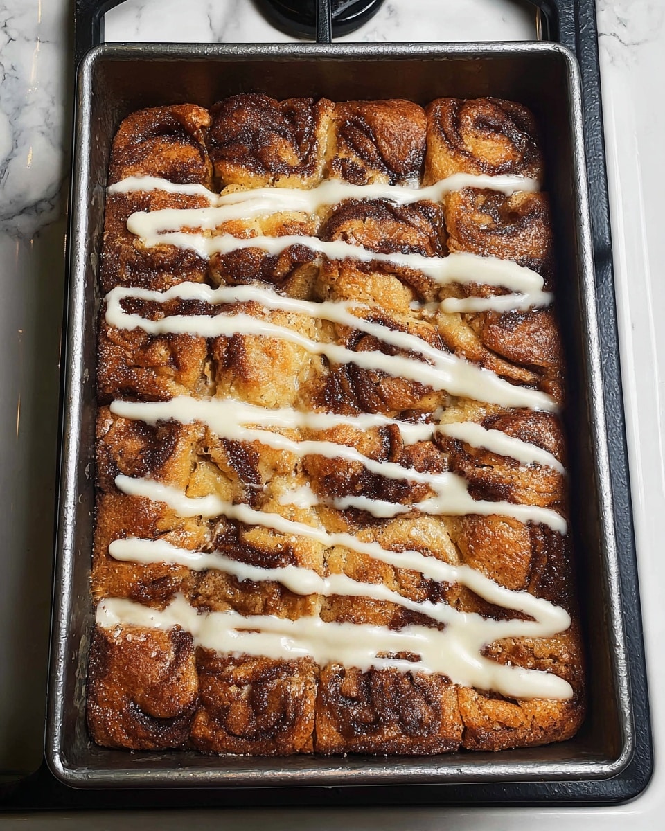 A rectangular metal baking pan holds a dessert with one thick, uneven layer of toasted golden brown and dark brown swirled bread pieces or dough, showing varied textures from soft to crisp. The top is decorated with irregular white icing lines drizzled across the surface in a scattered pattern. The pan is placed on a white marbled stove top with black stovetop elements visible around. photo taken with an iphone --ar 4:5 --v 7