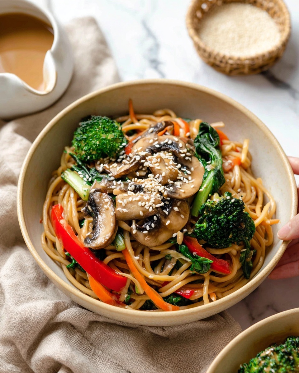 The image shows a close-up of a bowl filled with stir-fried noodles topped with vegetables and sesame seeds. The bottom layer is long, light brown noodles mixed with thin orange carrot strips. On top of the noodles, there are bright green broccoli florets, dark green spinach leaves, thin red bell pepper slices, and light brown sliced mushrooms sprinkled with small white sesame seeds. The bowl is light beige and sits on a soft beige cloth with a small cup of light brown sauce nearby. The background is a white marbled surface with a small basket holding a white bowl with light grains inside. Photo taken with an iphone --ar 4:5 --v 7