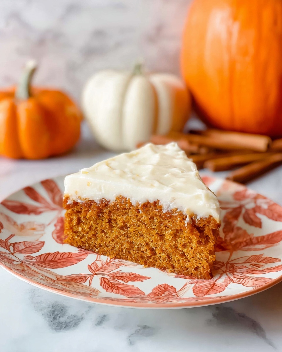A slice of pumpkin cake with one thick layer of orange-brown cake at the bottom and a thick creamy white layer of frosting on top, slightly textured, sits on a white plate with a large leaf pattern in warm red and cream colors. In the background, there is a white marbled surface, two pumpkins—one bright orange and one white—and cinnamon sticks, creating a cozy fall theme. Photo taken with an iphone --ar 4:5 --v 7