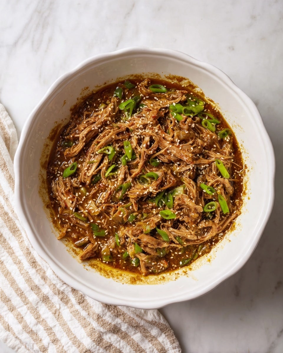 In a white bowl with a slightly scalloped edge, there is a mixture of shredded meat in a thick brown sauce. The shredded meat has a fibrous texture and is generously mixed with small pieces of bright green sliced scallions scattered throughout. Some white sesame seeds are visible on top of the sauce, adding a bit of contrast and texture. The bowl sits on a white marbled surface, with a beige and white striped cloth placed beside it. Photo taken with an iphone --ar 4:5 --v 7