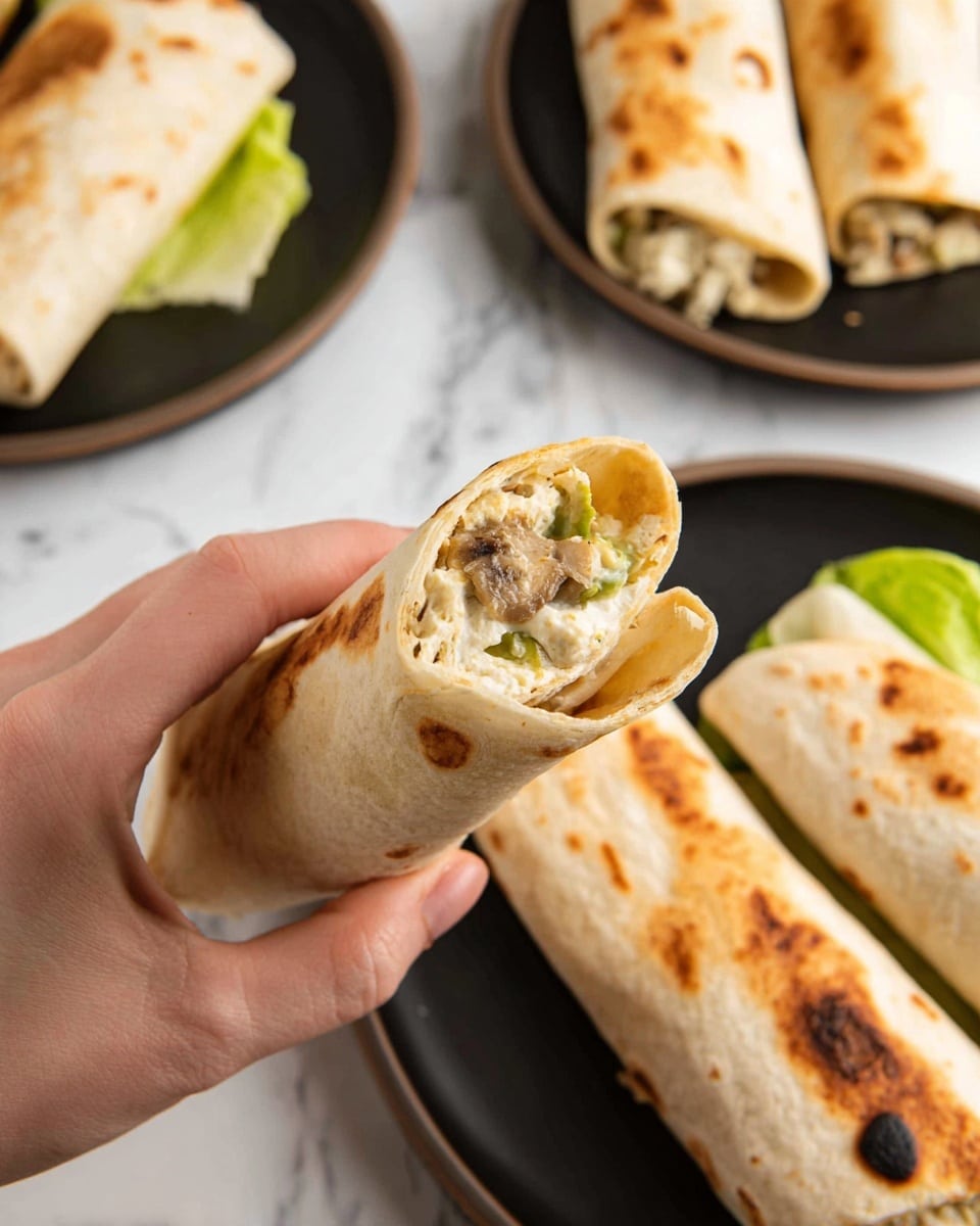 A close-up view of a woman's hand holding a toasted rolled wrap filled with a creamy mixture of soft white cheese and light brown bits, possibly meat or mushrooms, with some green vegetable pieces inside. The toasted wrap is light golden brown with some darker spots. In the background, there are black plates on a white marbled surface, holding several more similar toasted wraps, and one plate also has a green lettuce leaf underpinning some wraps. Photo taken with an iphone --ar 4:5 --v 7